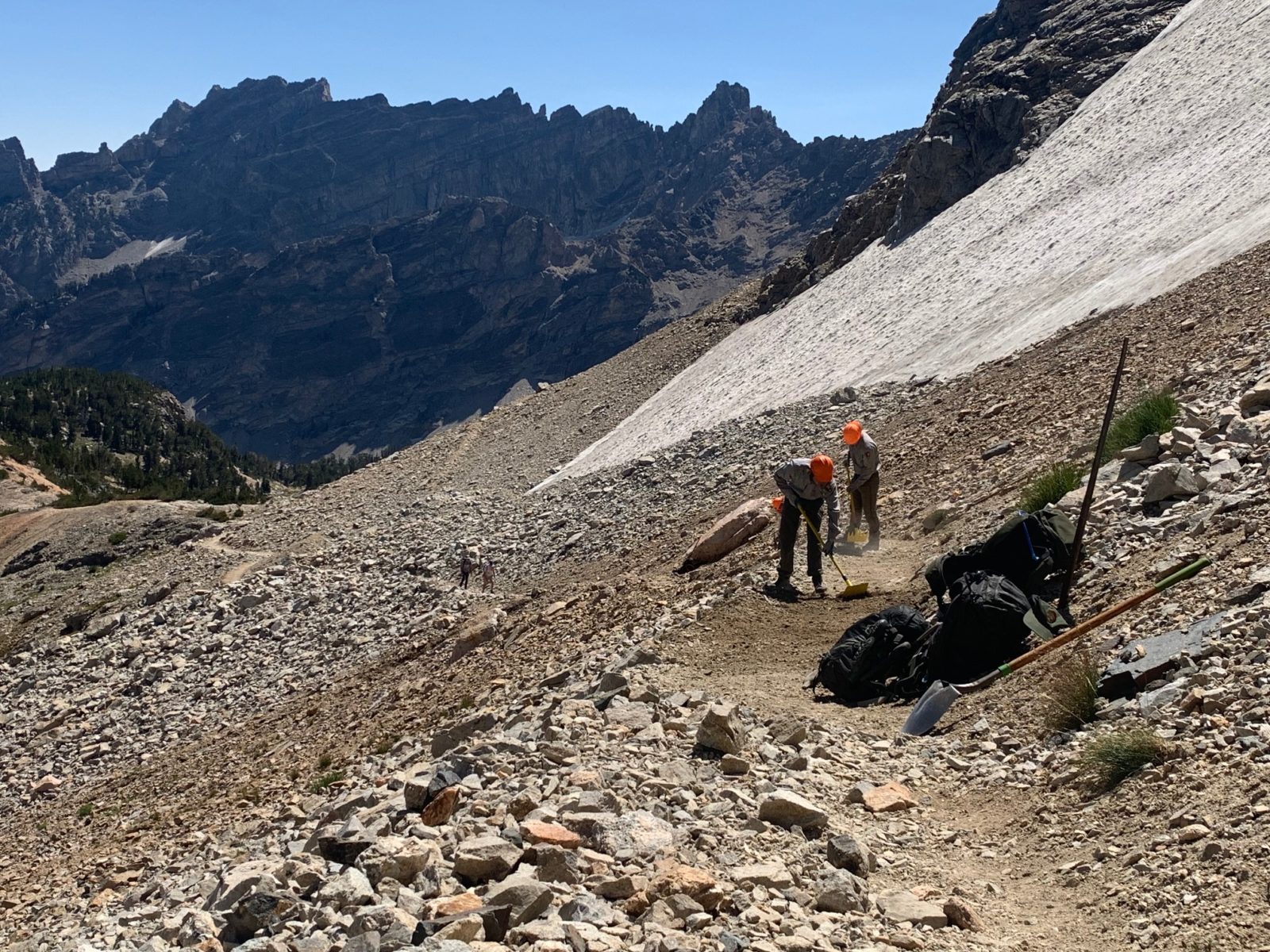 Trail crew members use hand tools to re-bench a section of loose, washed-out trail along the divide.